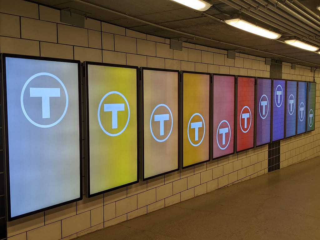 A line of ad displays with each screen a different color and the MBTA logo