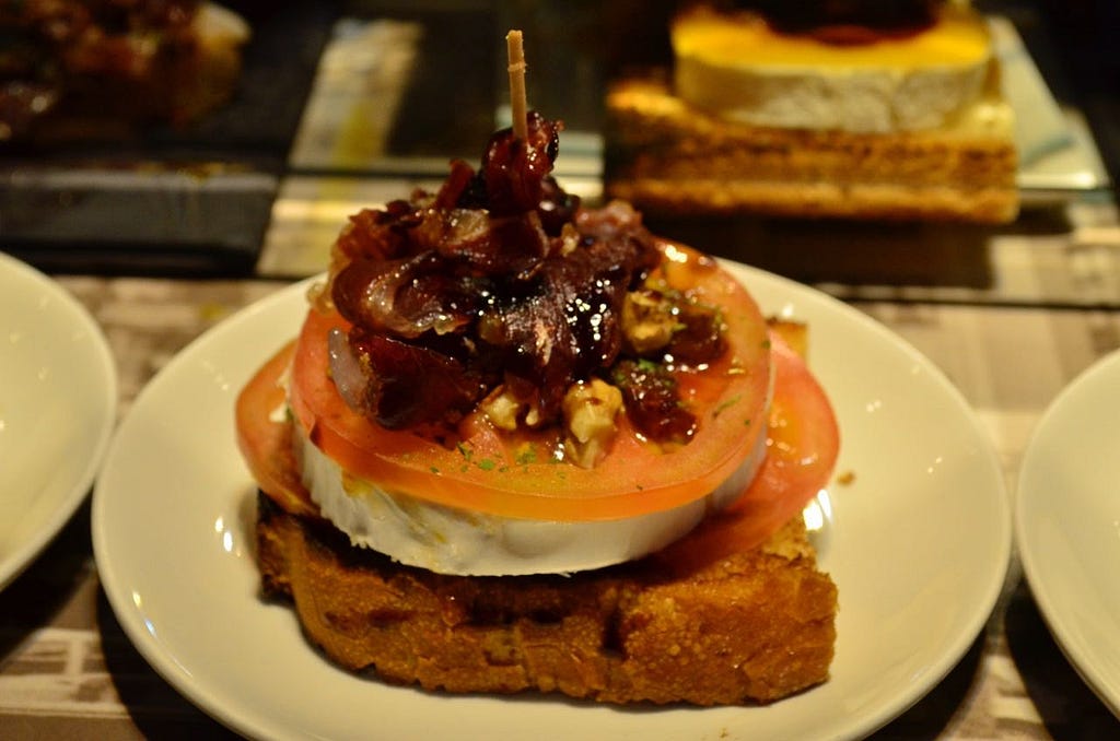 Close up of a delicious looking appetizer, with caramelized onion, tomato, and goat cheese on a slice of baguette