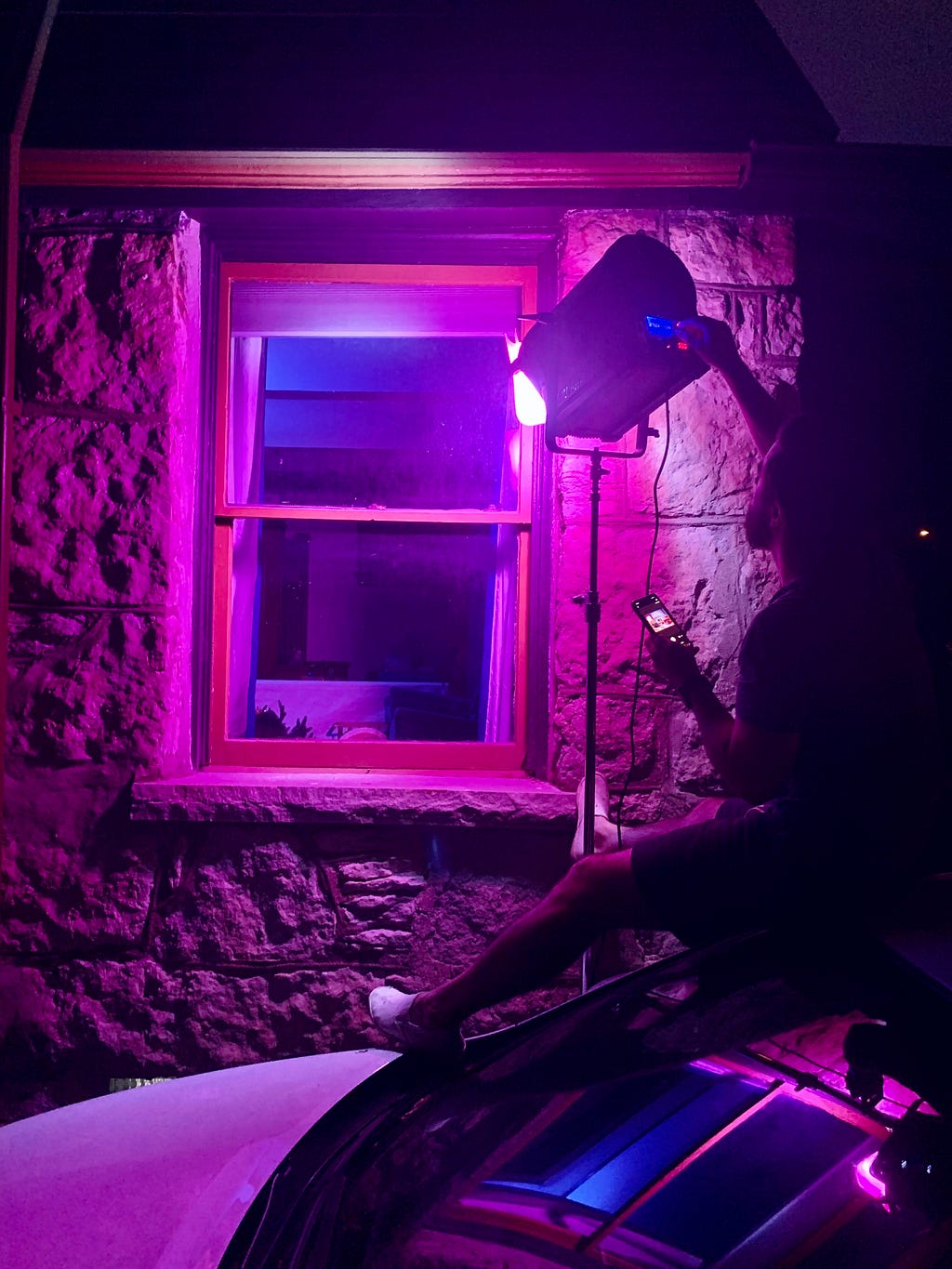 Refe sits on the roof of a car and shines a powerful pink light through the window of a house in the middle of the night.