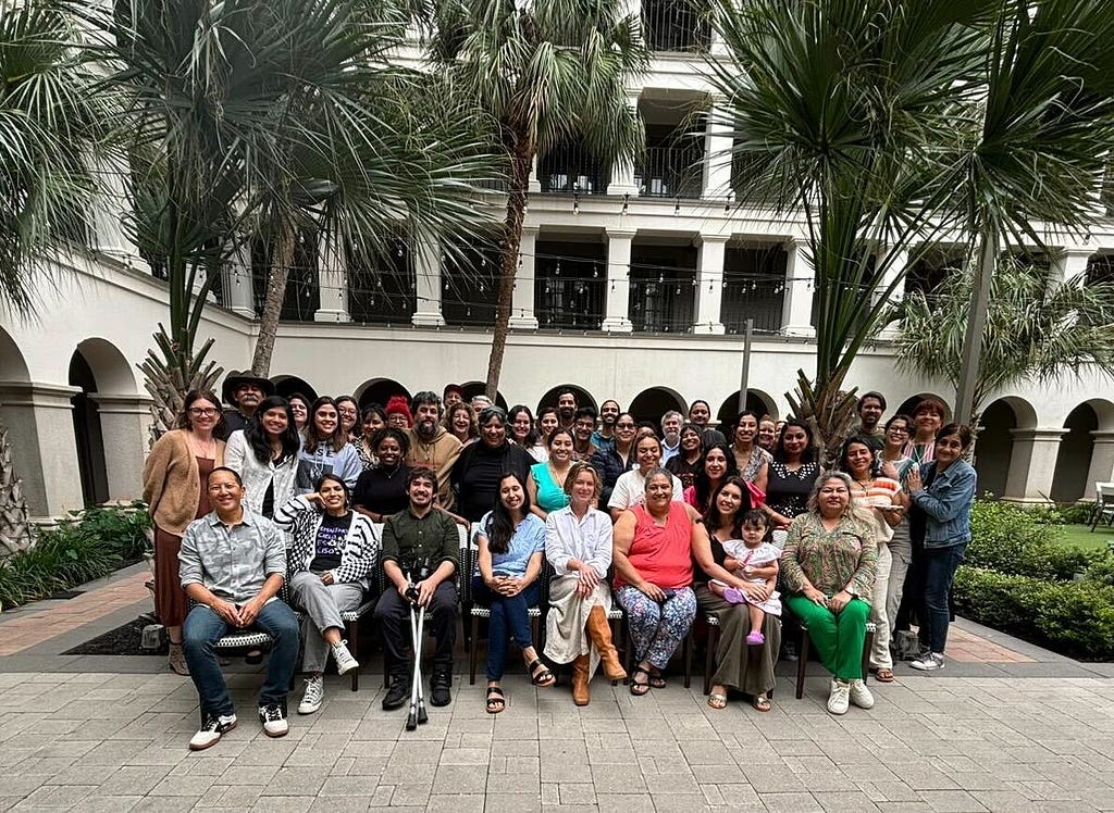 A large group of people, namely organizers and supporting folks involved in the immigrants rights and human rights movements, pose together in the patio of a hotel in San Antonio, Texas during a convening regarding Greg Abbott’s Operation Lone Star.