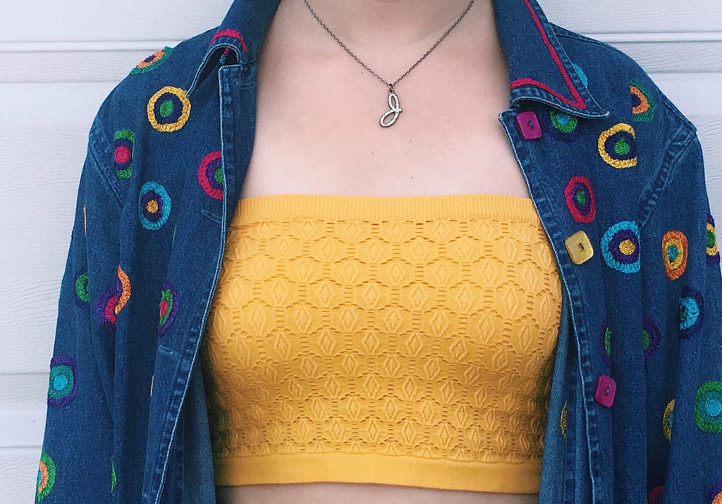 A yellow tube top underneath a denim jacket that has pink, blue, and green circles sewn onto it.