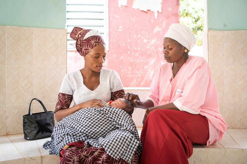 Two women gaze at newborn being held on the lap of one of the women.