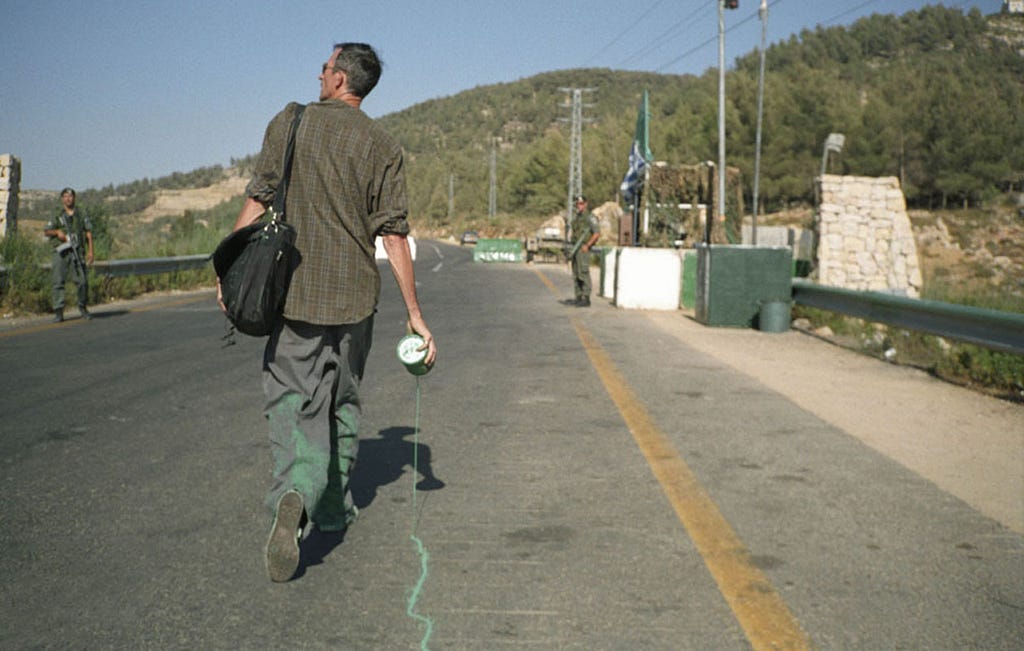 A man walking with a leaking can of green paint at the street