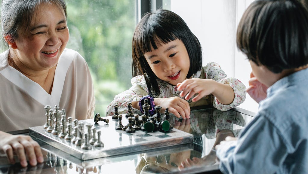 An older woman playing chess with two young children