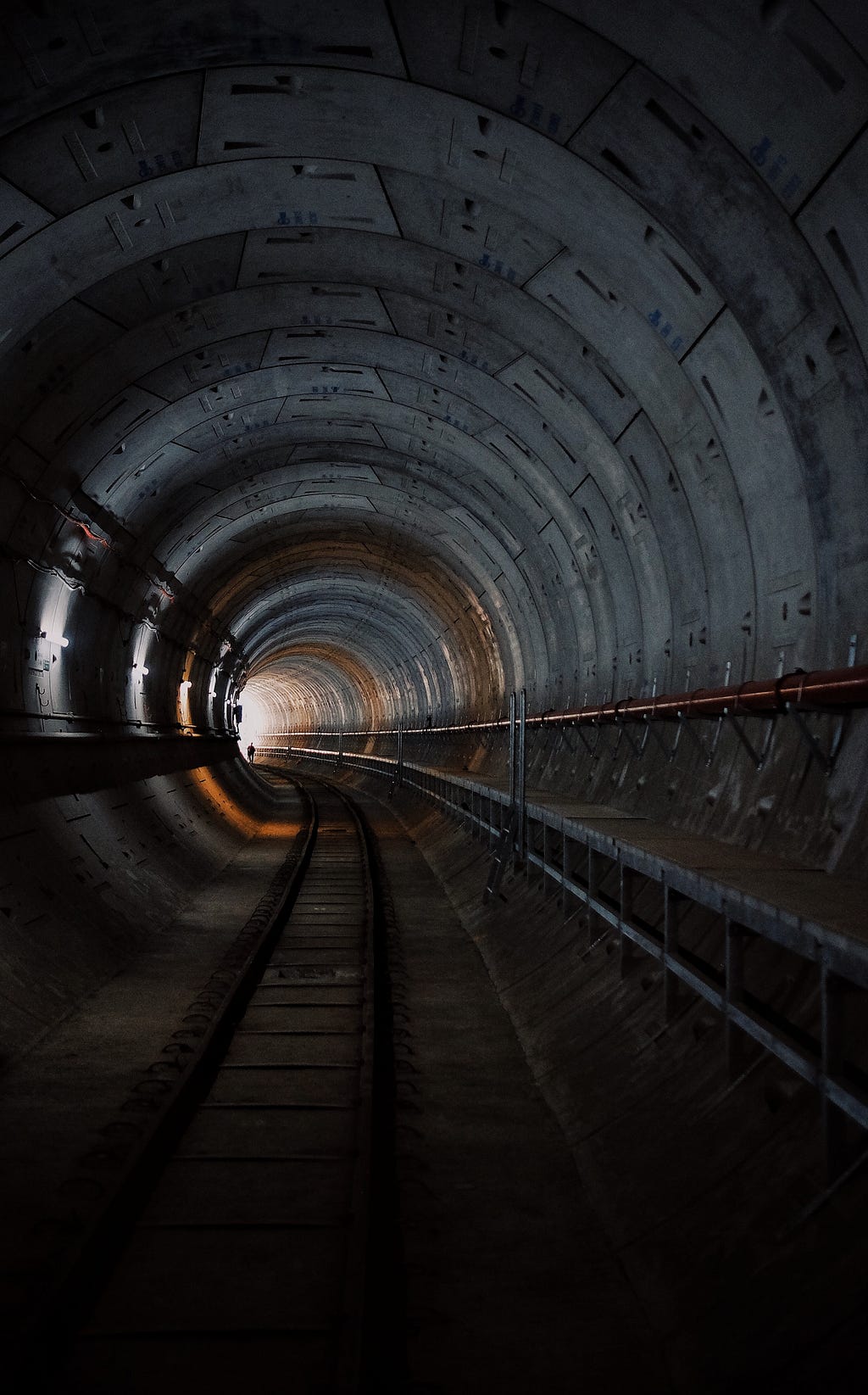 Man walks through a curving railway tunnel and find the light on the other side