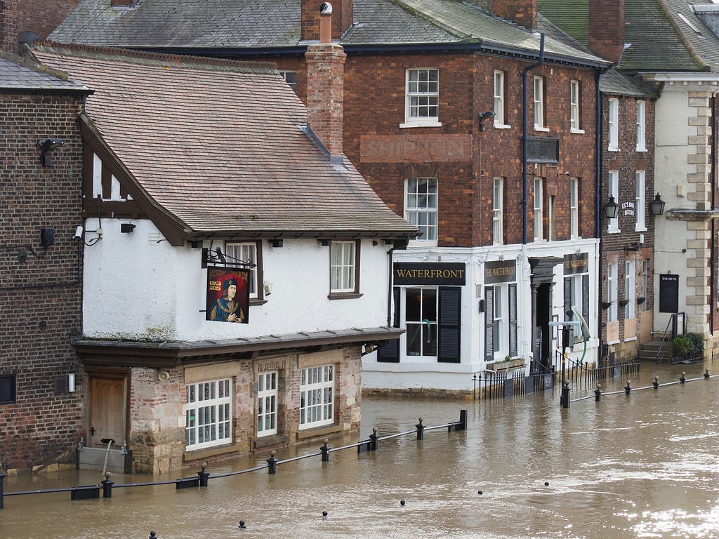 Street in a historic town with low rise buildings partially submerged in flood waters.