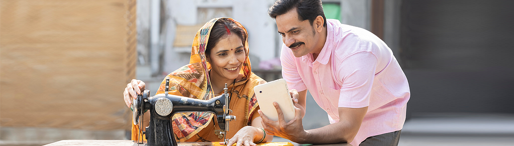A man and woman sit at a table with a sewing machine, showcasing the impact of digital marketing on India’s rural communities.