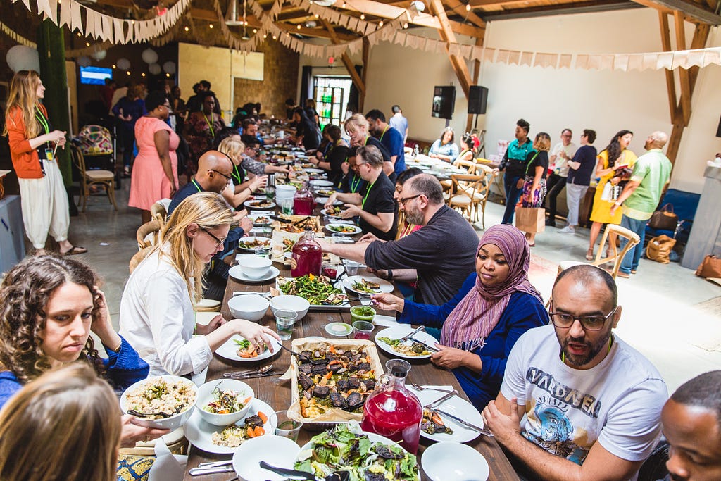 Entertain Change attendees sitting on two sides of a long table, eating and talking.