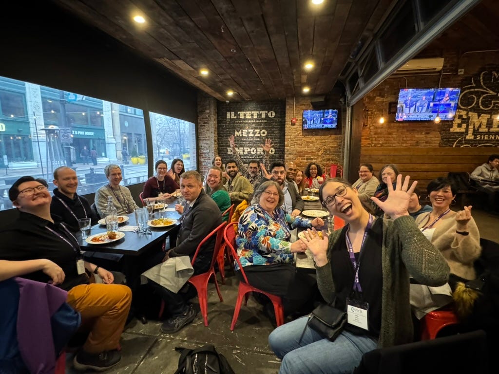 25 authors and editors joining together for a journal lunch, smiling at the camera, making weird faces.