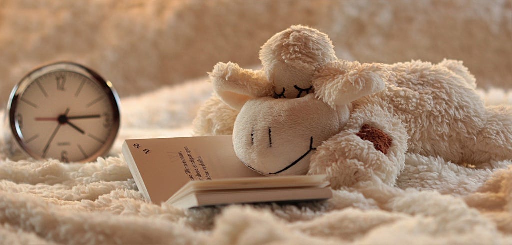 A cute image of a lamb plushie with closed eyes and an alarm clock.