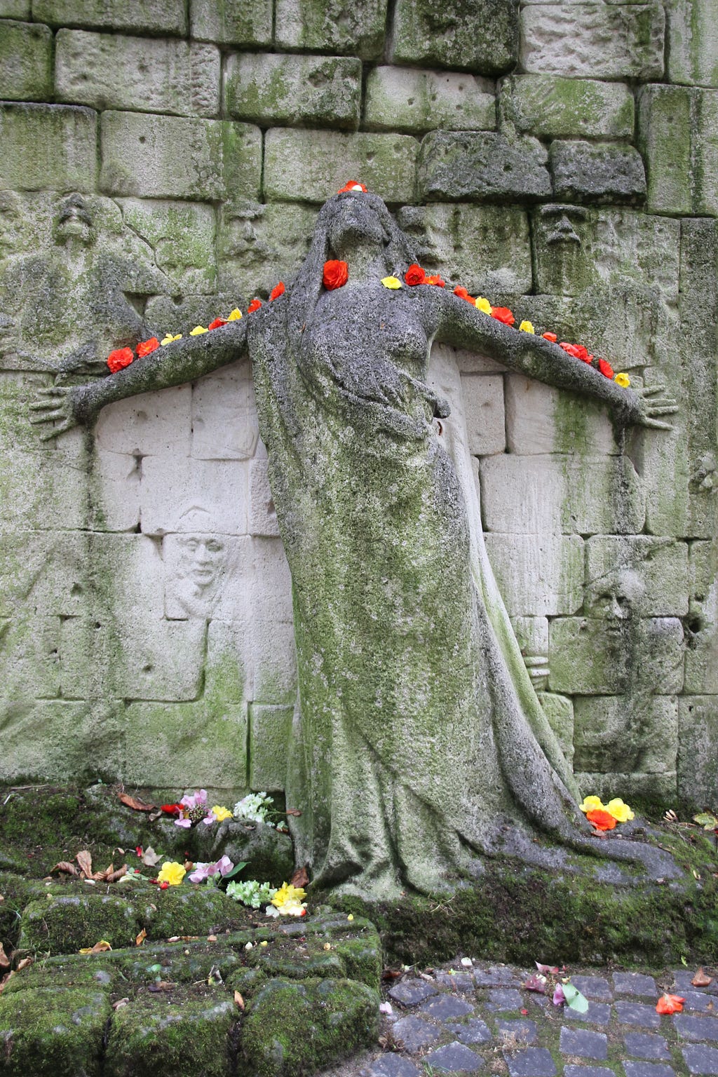 Red and yellow flower blossoms have been placed along the top edge of the arms of the female figure in relief, while the reliefs of other people seem to hover around her.