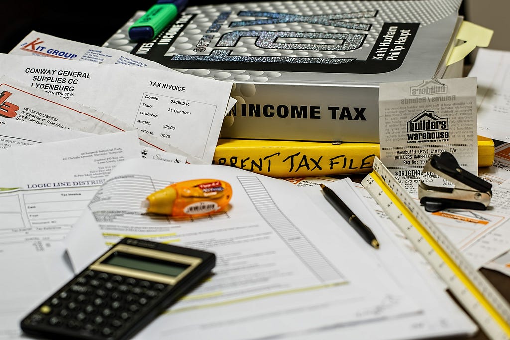 Income tax documents and books on a messy desk with a pen, calculator and liquid paper