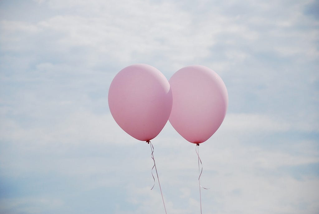Two pink balloons floating through a blue sky