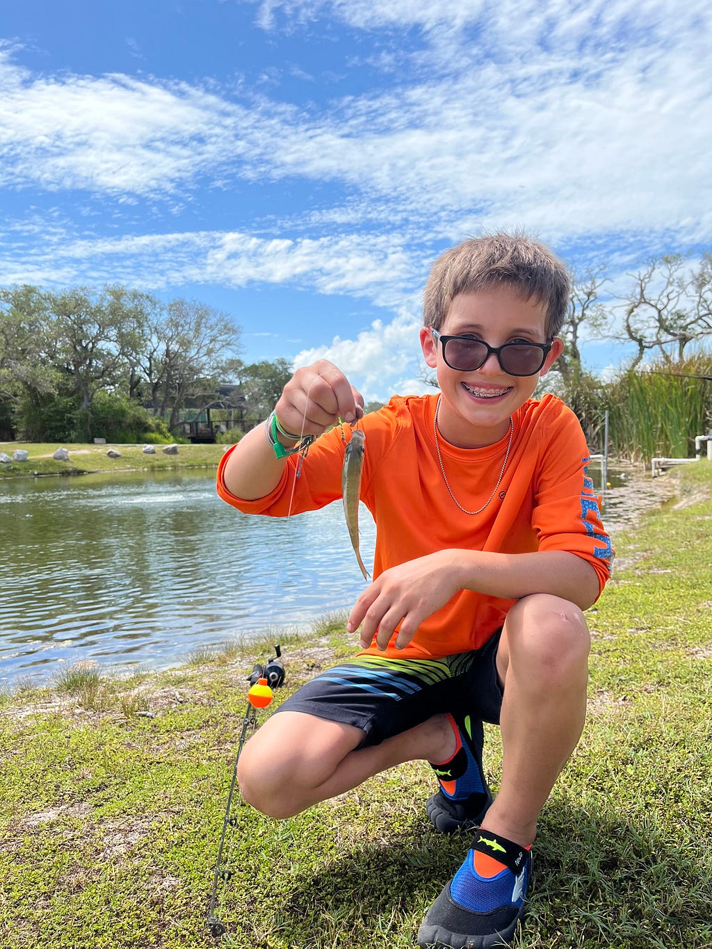 camper holds up fish that he caught at the fishing pond and smiles at camera