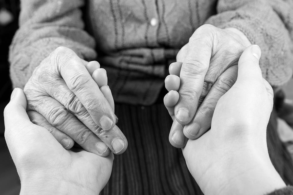 Hands of a young person holding those of  an older person. Photo by Obencem/Getty Images