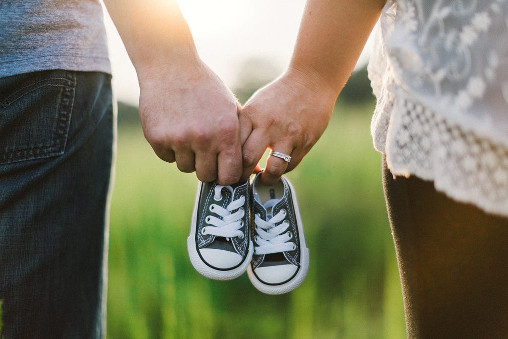 Hands of a woman and man holding a pair of tiny baby sneakers between them.