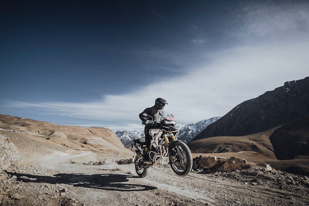 A man rides Triumph Motorcycles — Tiger 1200 & 800 on a hilly area, performing a stunt.