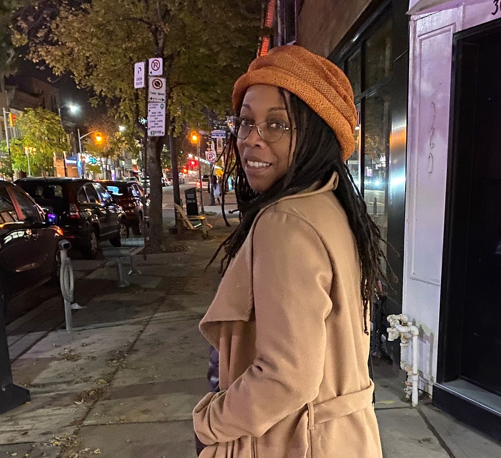 author on busy city street at night time, wearing orange hat