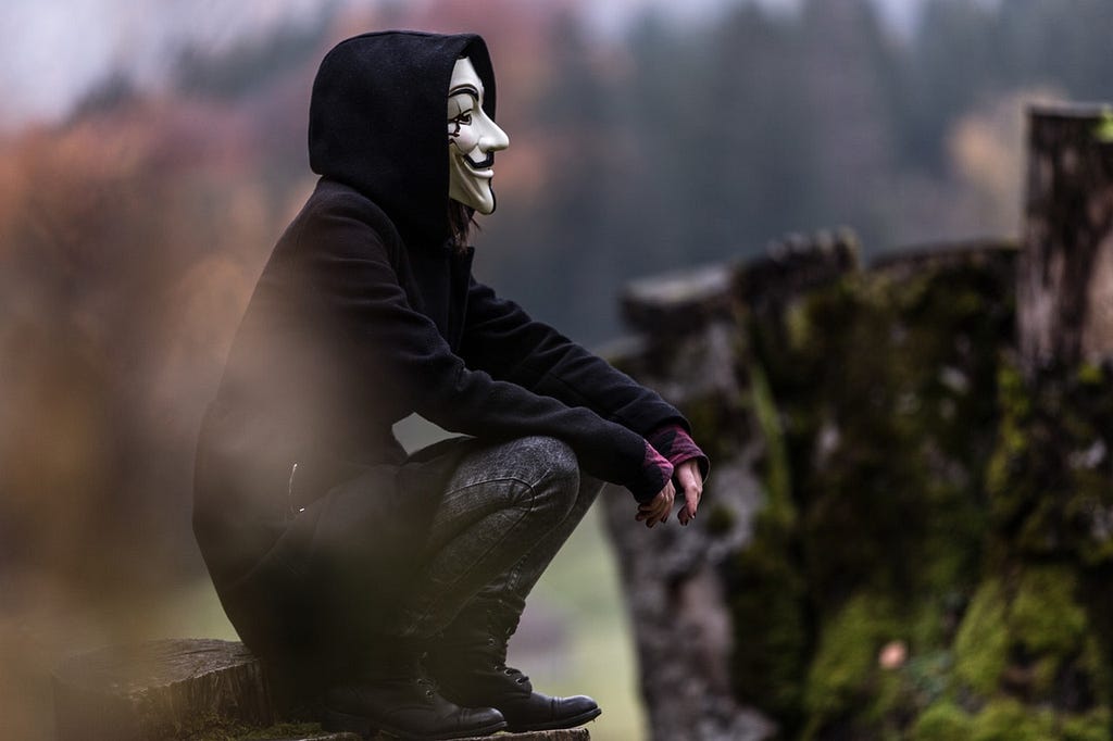 Boy with Guy Fawkes mask sitting down, looking to the distance