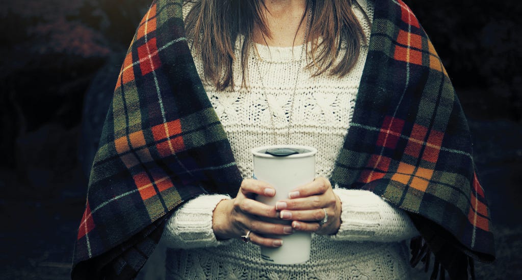 woman in a blanket holding a mug.