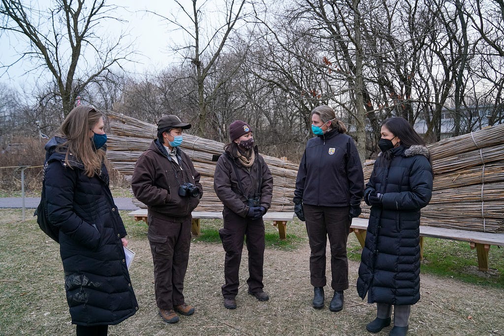 5 women wearing masks standing and talking next to two wooden benches on a national wildlife refuge