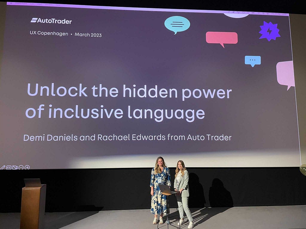 Demi Daniels and Rachael Edwards standing in front of a huge movie theatre screen showing the title slide of the workshop they are about to run. The title slide reads ‘Unlock the hidden power of inclusive language’. We look nervous, but excited!