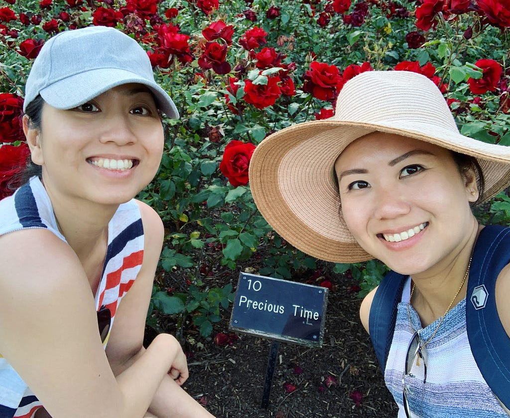 2 ladies with stripe shirts and a hat with a red rose brush in the background