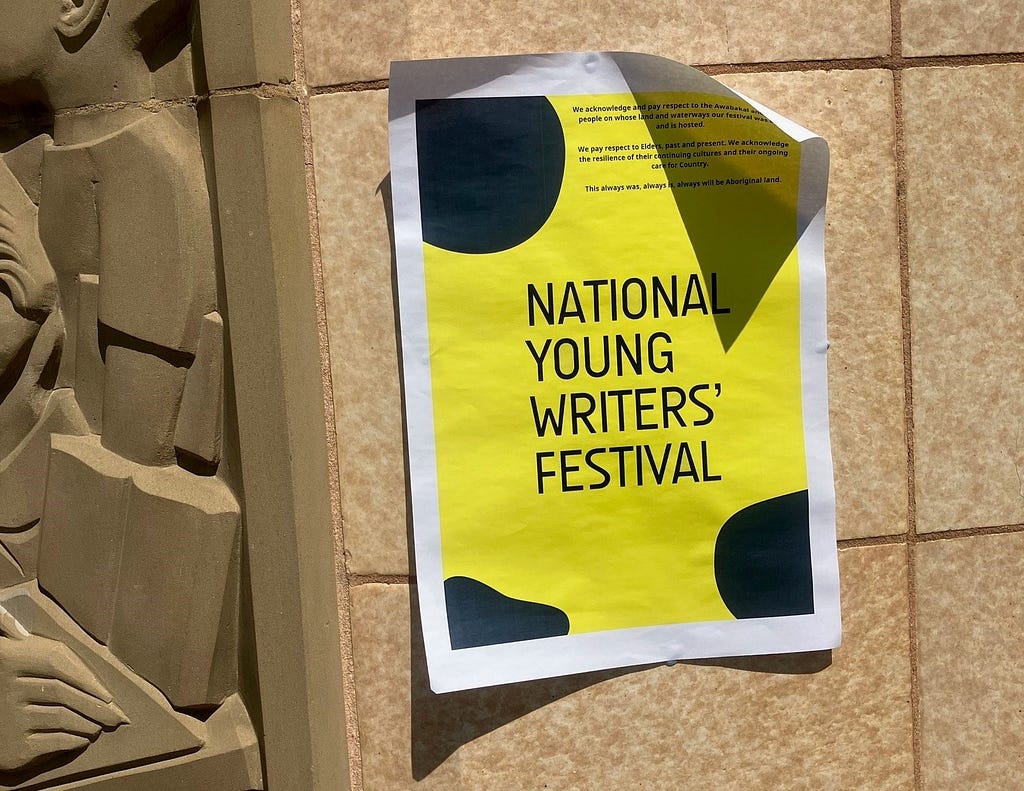 A paper sign advertising “National Young Writers’ Festival” blu-tacked on a sandstone building