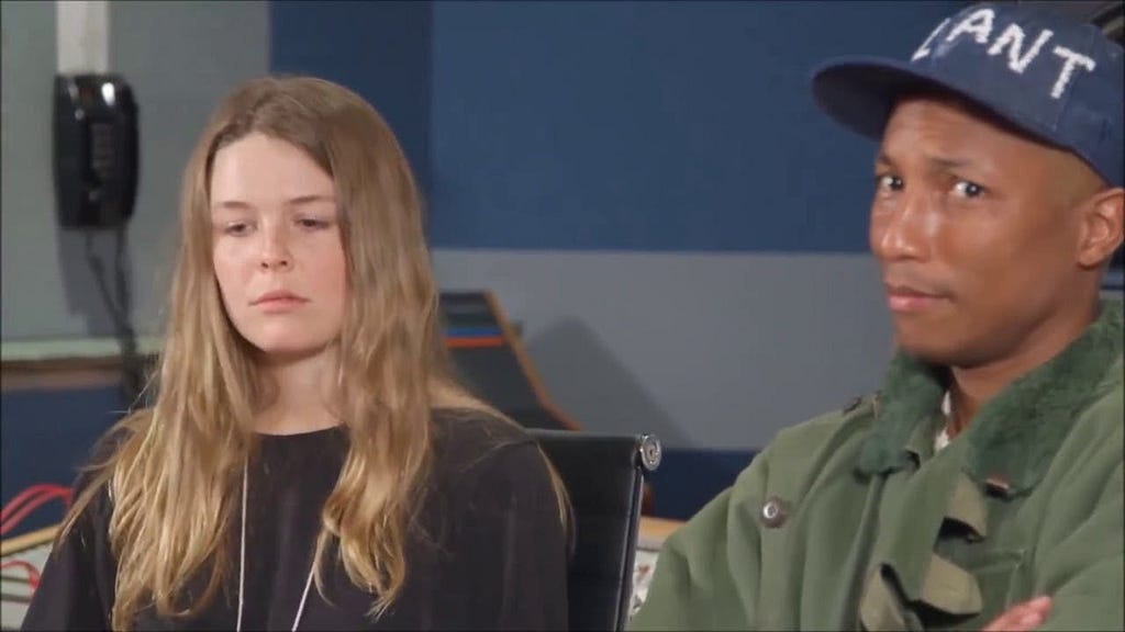 Maggie Rogers looks solemnly at the floor, while to our right, Pharrell Williams looks surprised towards the camera.