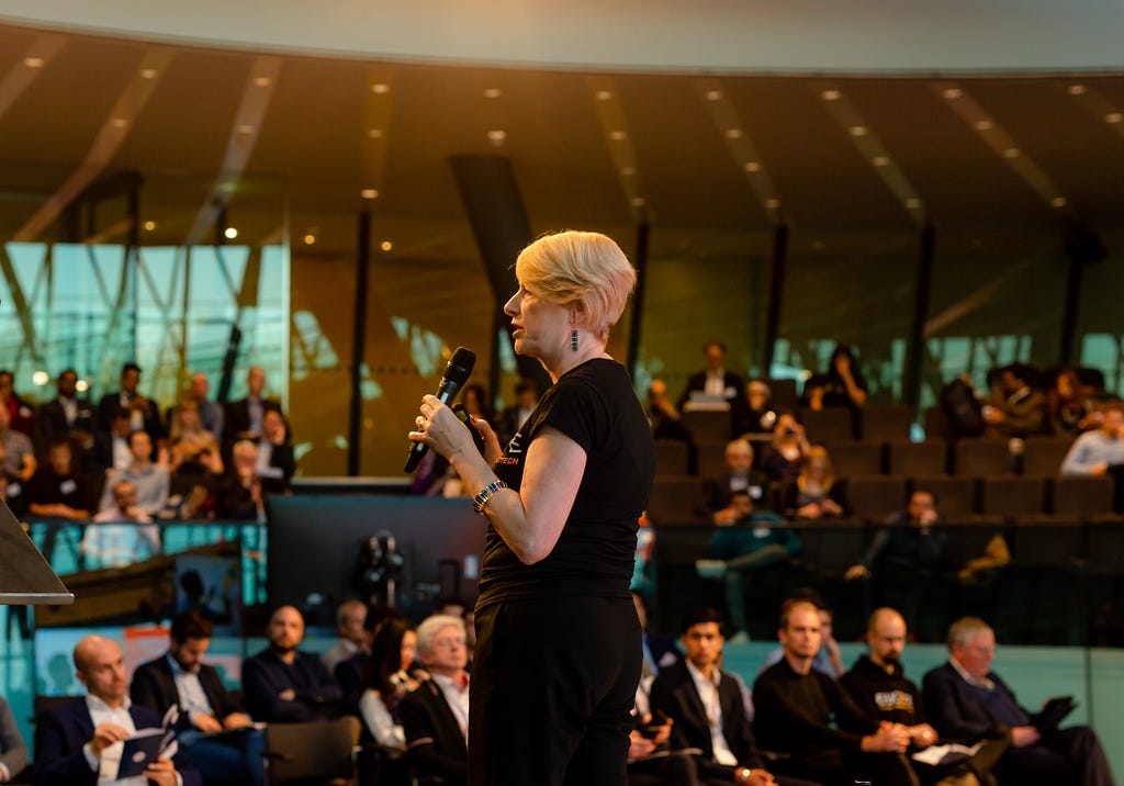 Professor Rose Luckin, Director of EDUCATE, stands with a microphone in front of a large audience at London’s City Hall