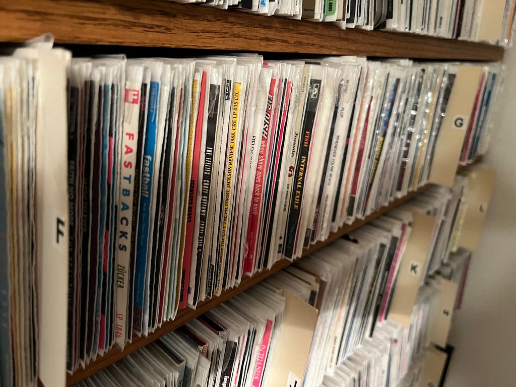 Shelf of wall unit with CDs in poly sleeves and lettered cards separating artists by first letter.