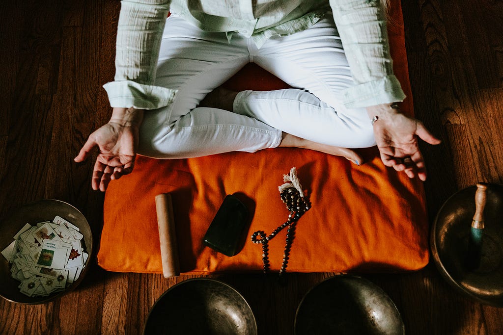 Woman sitting crossed-legged on the floor in a meditation position with singing bowls around her.