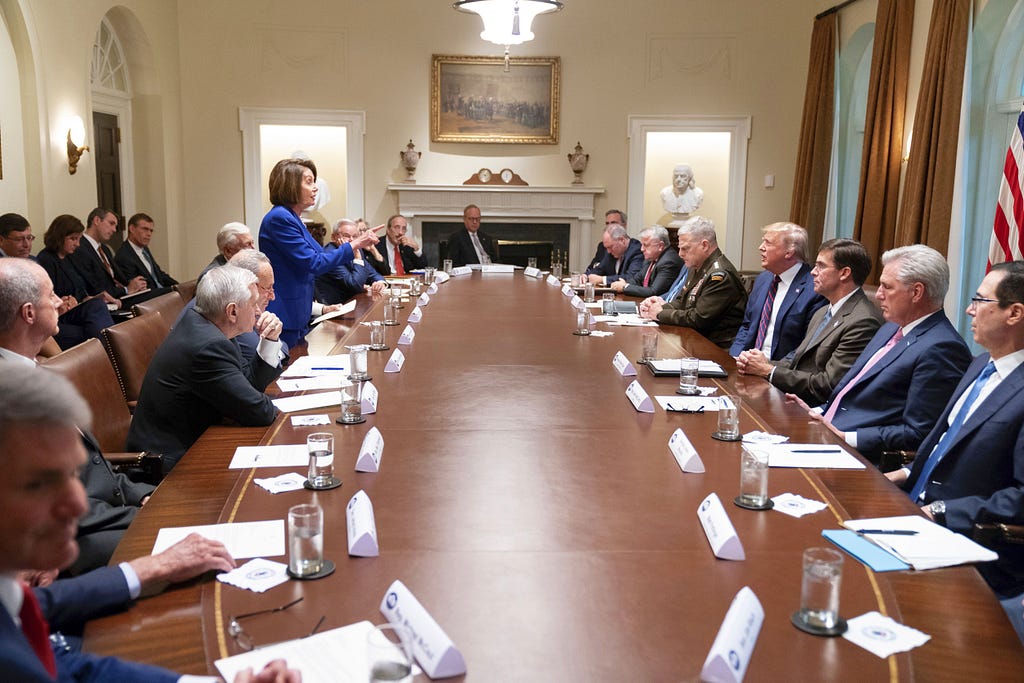 Speaker Pelosi wags her finger at then-President Trump at a congressional meeting where she is the only woman at the table, and the only person standing up. Trump is angry and all the men appear submissive.