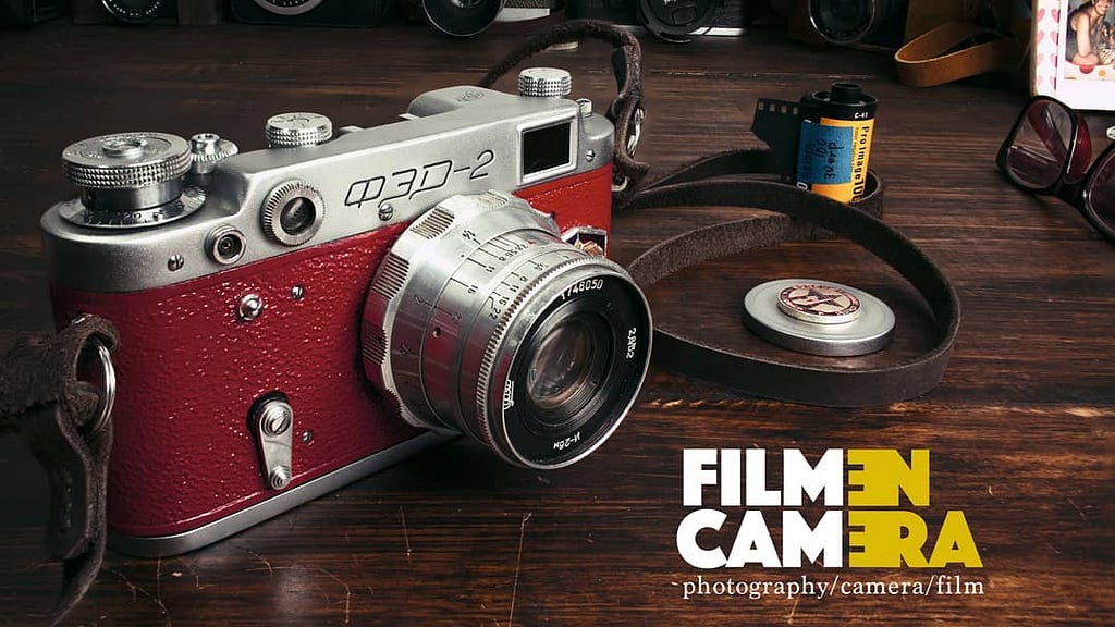 A FED2 soviet rangefinder camera on a wooden table alongside a roll of 35mm film cartridge.