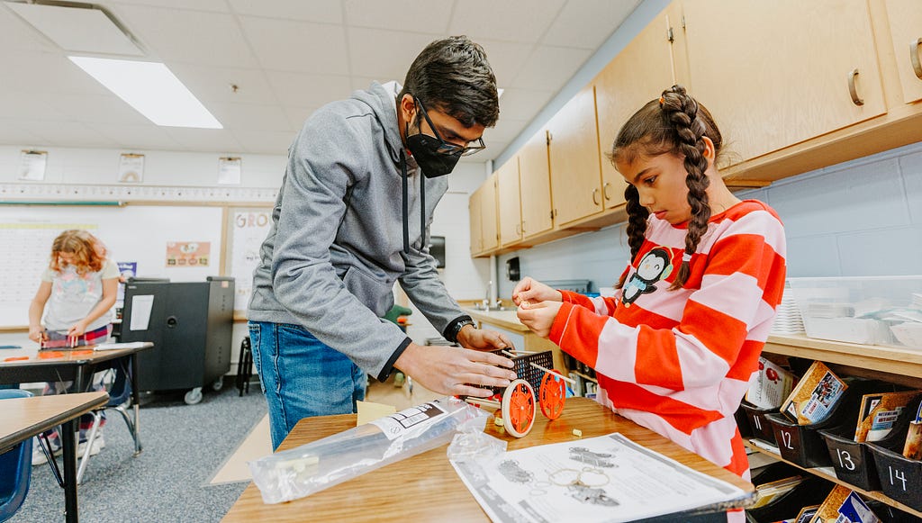 Rohan Tatineni helps a student assemble her rubber-band powered car.