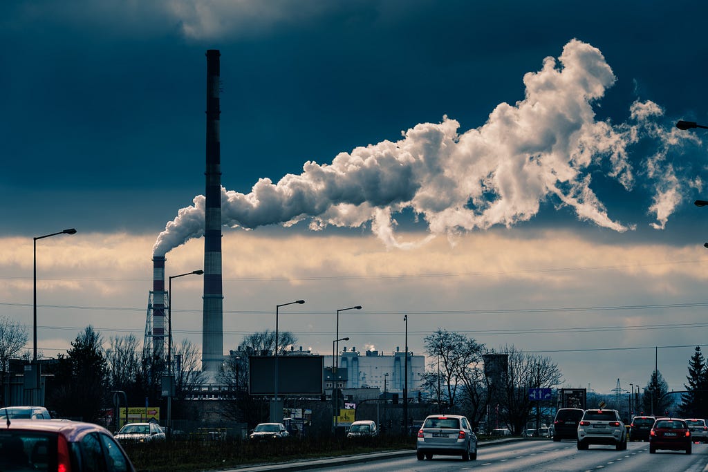 Two tall chimneys pouring thick white smoke over a busy motorway. Blue grey colours. Called Time to Change.