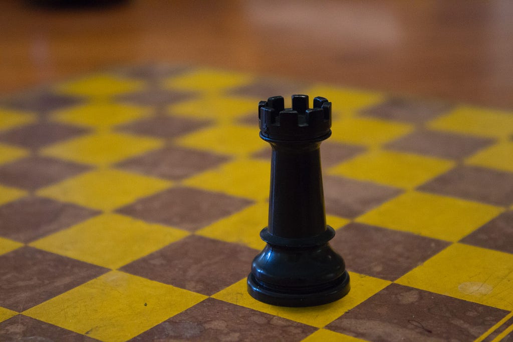 Black castle chess piece on an empty brown and yellow checkerboard