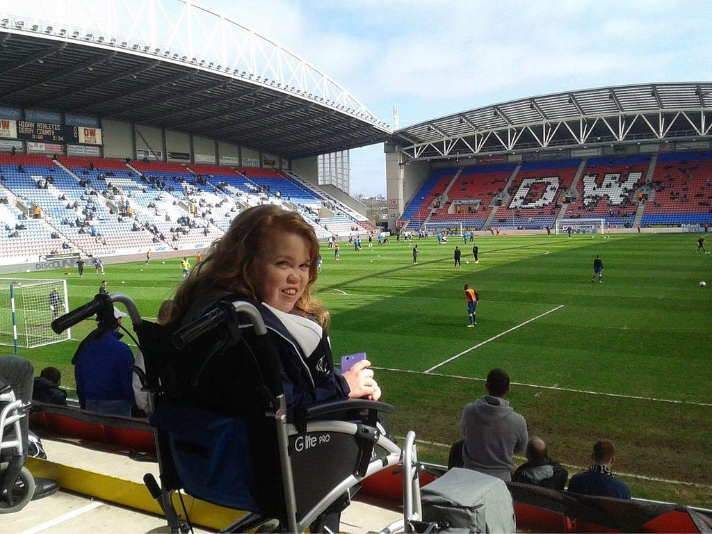 Alex in wheelchair smiling in front of pitch
