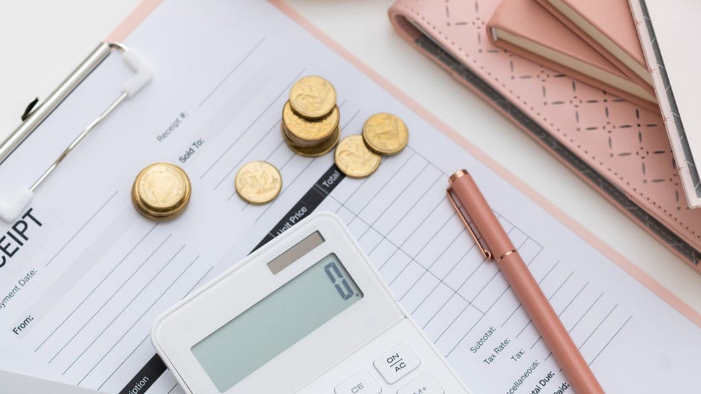 receipt on clipboard with coins and a calculator sitting on top