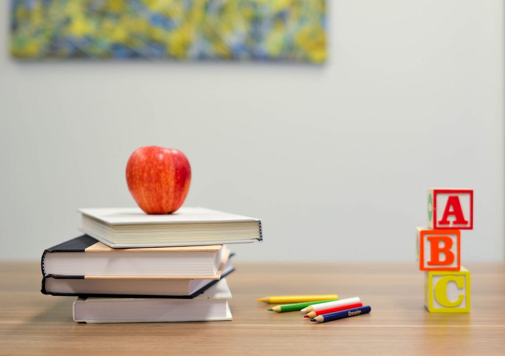 A teachers desk with books, an apple, and ABC blocks.