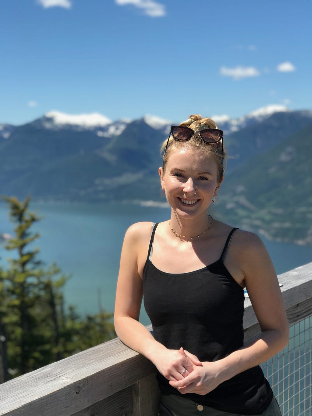 Hannah Hennig smiles as she leans against a railing with a lake and mountains in the background.