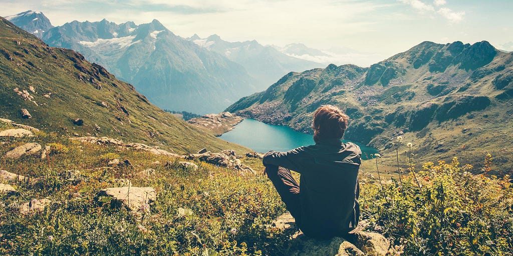 Silent man sitting on a mountainside looking at a lake