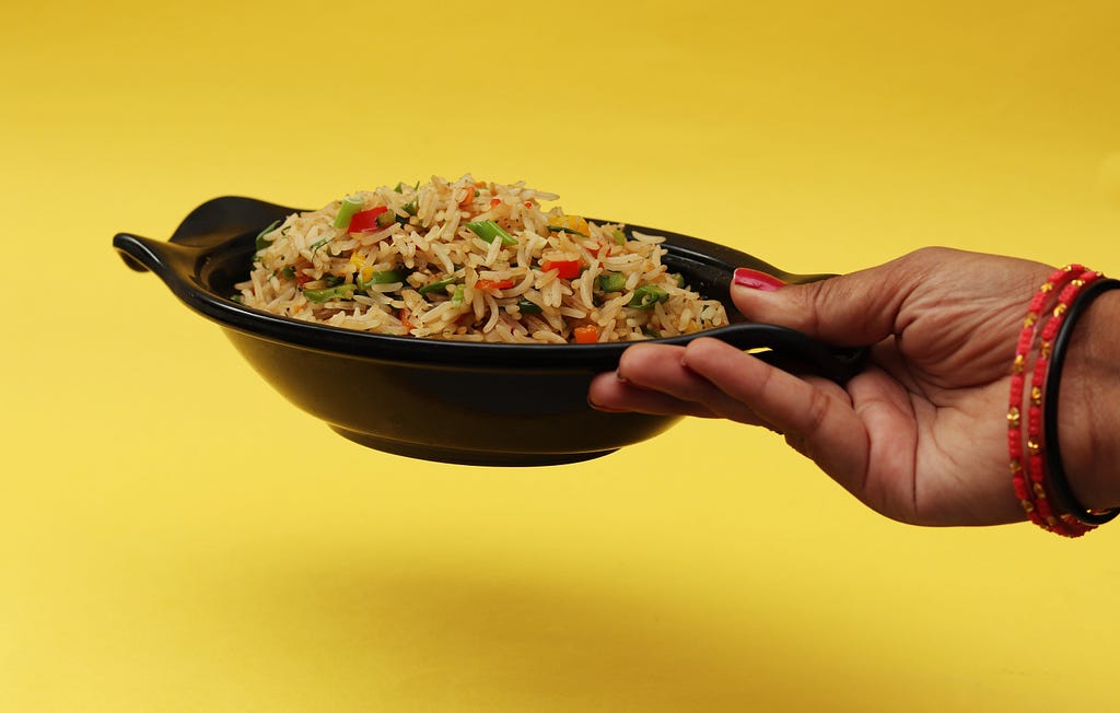 Woman’s hand holding a bowl of fried rice