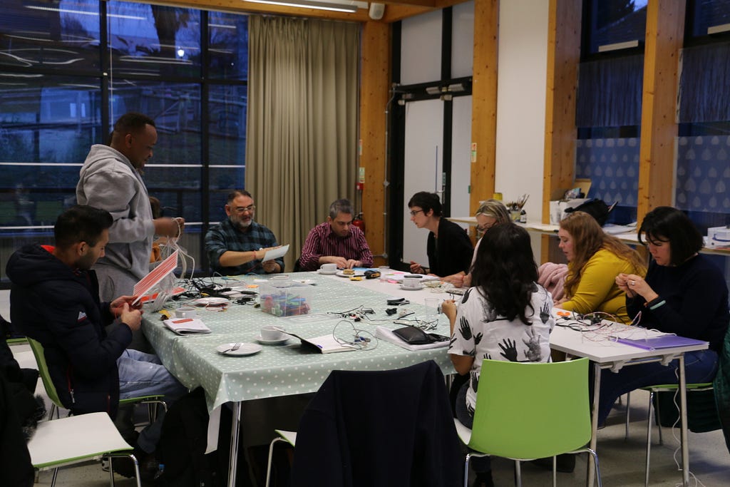 A group of people around a table weaving materials together.