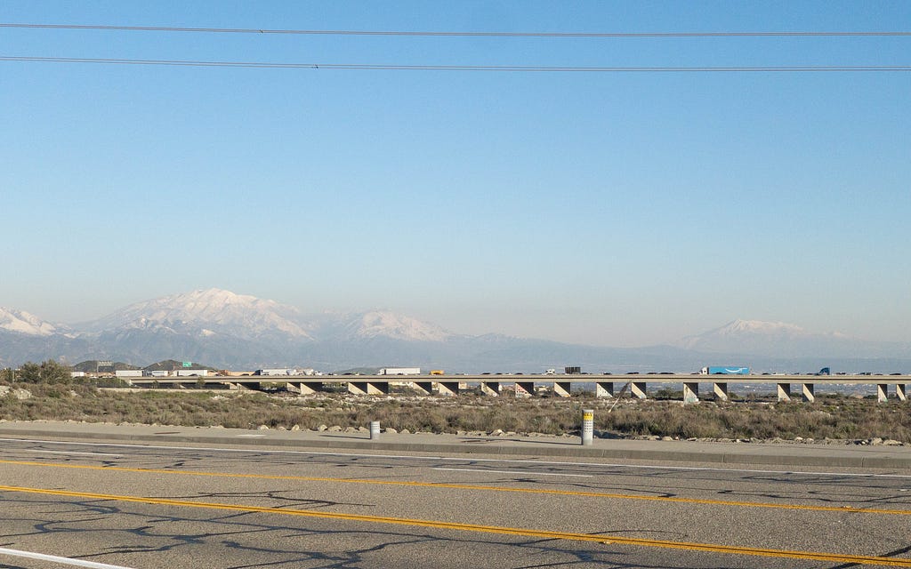 photo of an elevated highway above desert brush. Mountain range in the background