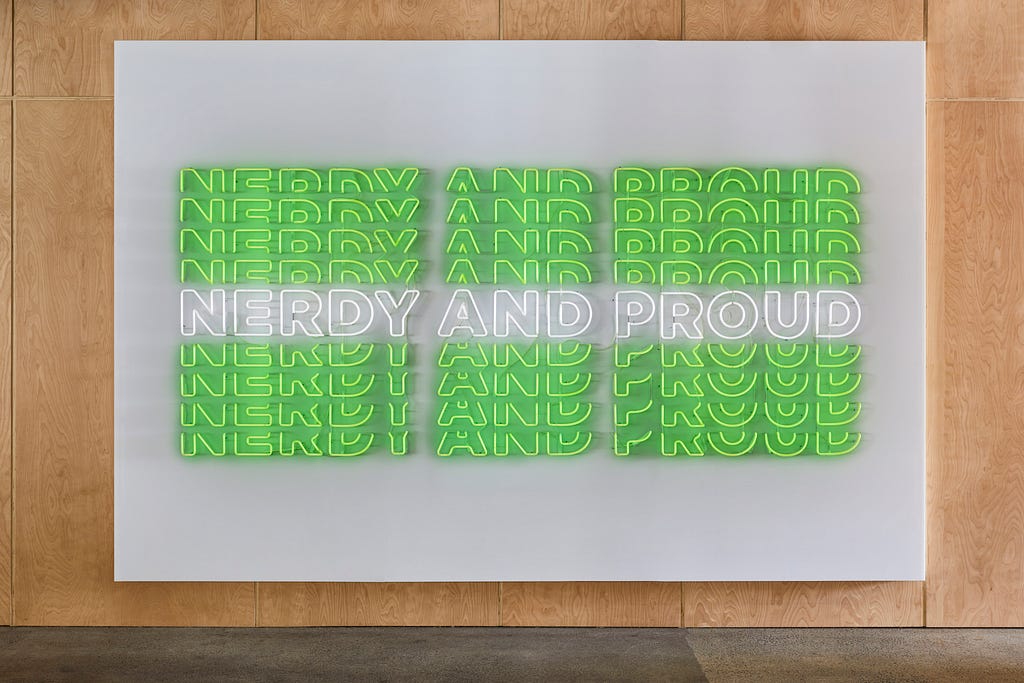 A large neon sign mounted on the wall, displaying the phrase “Nerdy and proud” in green and white all capital neon letters.