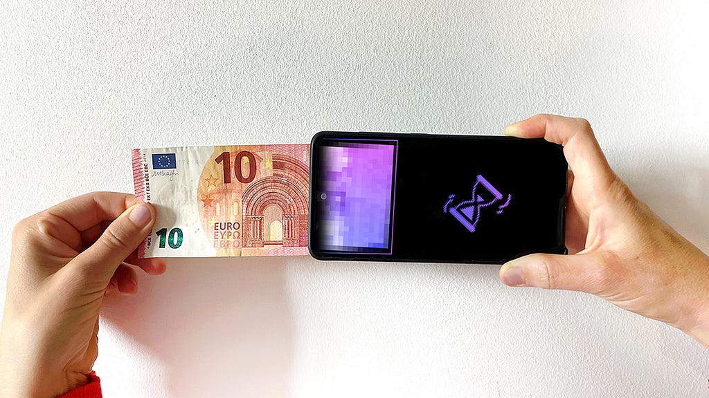 a hand pushes a 10euro note into a smartphone from left to right. on the screen of the smartphone is the end of the euro note in purple pixels — the fiat money is transformed into pixels. on the right side of the screen on a black background a digital hourglass is showing that this is being processed.