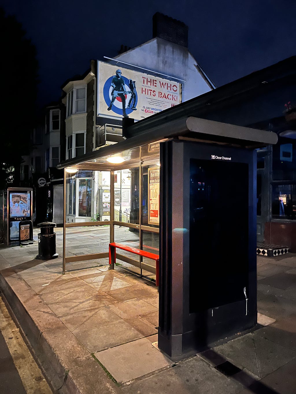 Photograph of a lit-up Hove bus stop at night, with a poster for a concert by The Who on the wall behind it.