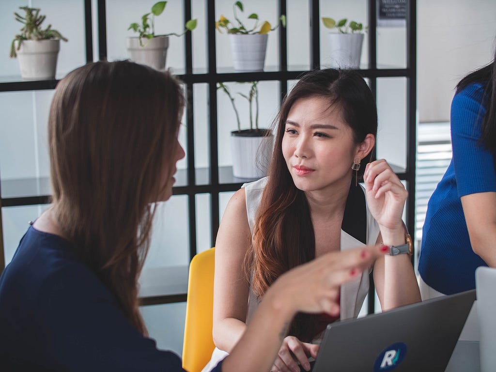 One woman explains information to another woman in a workplace.