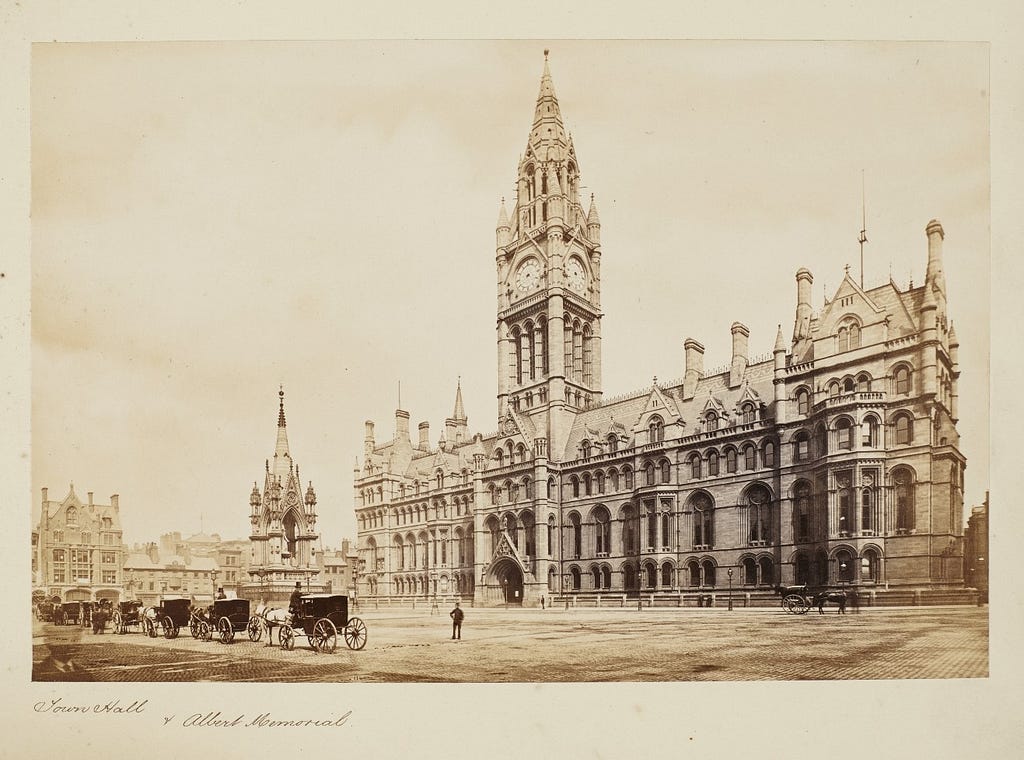 Exterior of Manchester’s neo-gothic Town Hall in Albert Square, with the Albert Memorial and a row of horse-drawn cabs (1877)